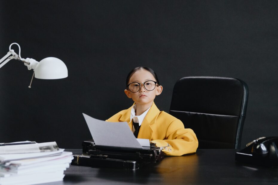 child with glasses sat at desk dressed in a suit