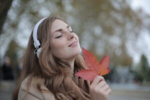 Woman wearing headphones, smiling whilst holding a leaf. 500 things to be grateful for.
