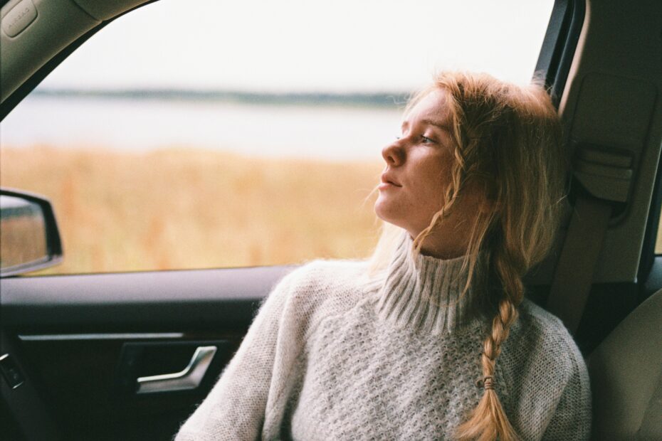 ways to improve your mental wellbeing Girl wearing cream-coloured jumper staring out of a car window.