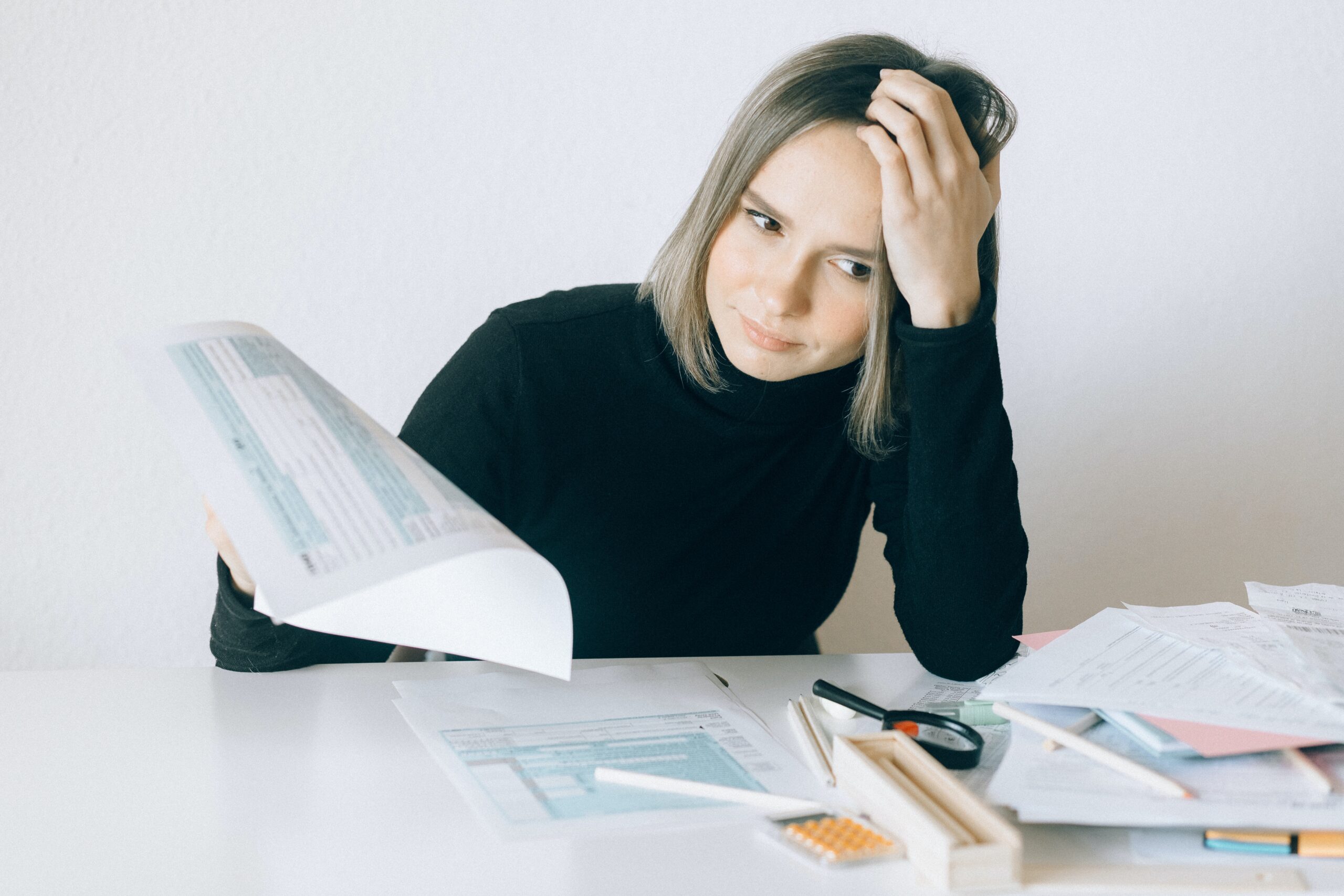 money quiz income tax - woman with shoulder length hair wearing black, staring at tax forms with her head in her hand.