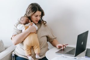 Money quiz UK national insurance - mum holding newborn baby sat at laptop
